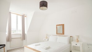A bedroom with a bed, bedside tables, a window with curtains, a ceiling light, and a wall-mounted mirror. - The Links 08, Amazing Location- Food, Drinks, Surf, & Golf! - 8 (Lahinch)