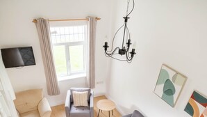 A modern living room with a grey sofa, a wooden coffee table, and a grey armchair. A TV is mounted on the wall, and there is a window with curtains. - The Links 08, Amazing Location- Food, Drinks, Surf, & Golf! - 8 (Lahinch)