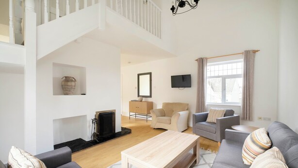 A spacious living room with a high ceiling, a fireplace, a television, and a comfortable seating area with sofas and a coffee table. - The Links 08, Amazing Location- Food, Drinks, Surf, & Golf! - 8 (Lahinch)
