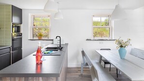A modern kitchen with a central island, two pendant lights, a built-in oven, and a window with a view of greenery. - The Play School, The Play School (Miltown Malbay)