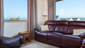Una habitación con sofá de cuero, una pequeña mesa de madera y vistas al mar a través de amplios ventanales.
