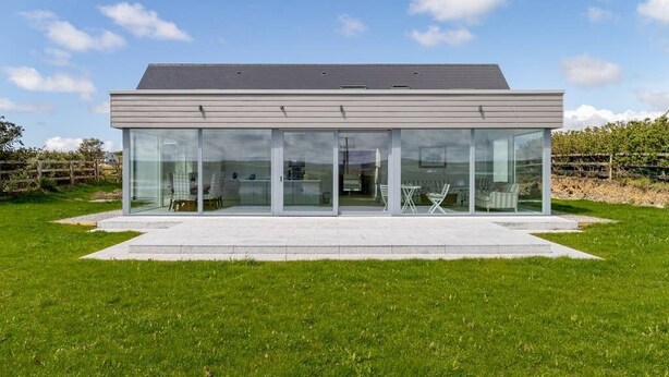 Ein modernes Haus mit Flachdach, großen Glasfenstern und einer gepflasterten Terrasse.