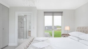 Ein modernes Hotelzimmer mit einem großen Bett, einer begehbaren Dusche und Blick ins Freie.