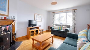 A living room with a fireplace, a television, a sofa, and a window with curtains. - Summer Cove 10 (900m to Lahinch Beach) (Lahinch)