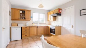 A compact kitchen with wooden cabinets, a white refrigerator, a stove, and a window providing natural light. - Summer Cove 10 (900m to Lahinch Beach) (Lahinch)