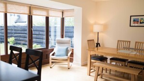 Un comedor con mesa y sillas de madera, un banco, una silla acolchada con cojín y una lámpara.