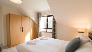 Un dormitorio con una cama grande, un armario, una ventana con cortinas y una lámpara de noche.