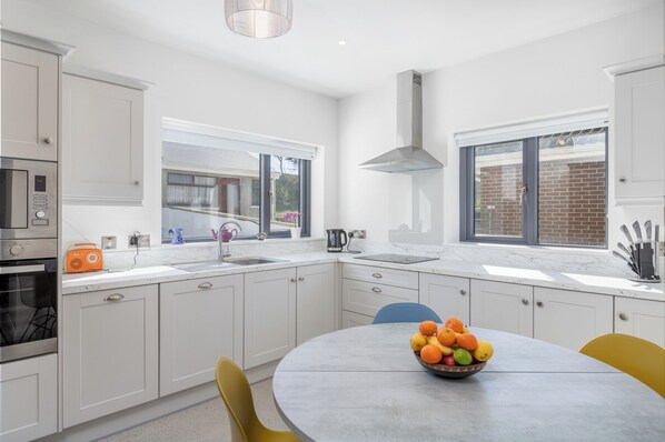 A modern kitchen with white cabinetry, a round dining table, and a bowl of fruit.
