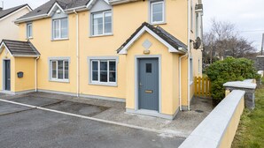 Un immeuble résidentiel de deux étages, avec une façade jaune, une porte grise et des encadrements de fenêtres blancs.