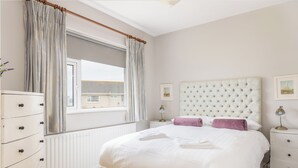 Een slaapkamer met een groot bed, een kaptafel, een nachtkastje, een raam met gordijnen en een radiator.