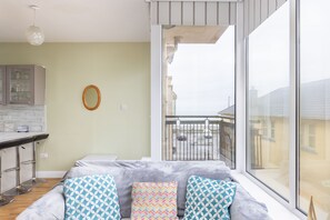 A modern apartment with a balcony, a kitchen area, and a seating area with patterned cushions.