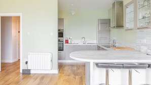 Moderni keittiö, jossa on keskeinen saareke, integroidut kodinkoneet ja näkymä viereiseen olohuoneeseen.
