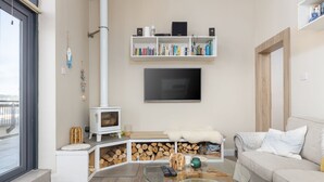 Un salon moderne avec une cheminée blanche, une table basse en verre, un canapé beige et une bibliothèque remplie de livres et d’objets décoratifs.