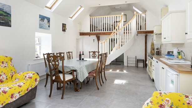 Ein Essbereich mit hoher Decke, Dachfenstern, einer Treppe und einer Küchenzeile mit weißen Schränken und einer Holz Arbeitsplatte.