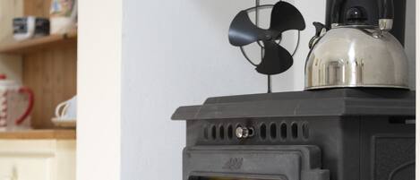 Un poêle à bois noir, avec une bouilloire posée sur le dessus, un ventilateur et une fenêtre.