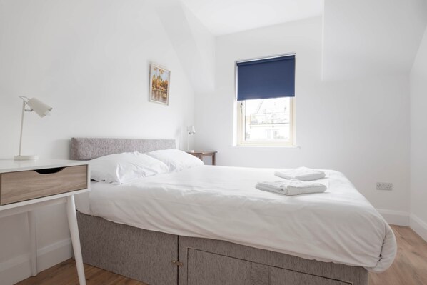 A bedroom with a bed, a desk, a lamp, a window with a blue blind, and a picture on the wall. - Cill Stuifin 15 - Beach Vibes! (Lahinch)