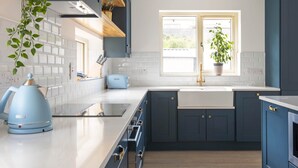 Et moderne køkken med mørkeblå skabe, en hvid bordplade og et vindue der lukker naturligt lys ind.
