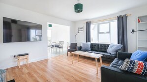 A modern living room with a flat-screen TV, a sofa, a coffee table, and a dining area with chairs. - Clochan Na Mara 15 (In Liscannor Village) (County Clare)