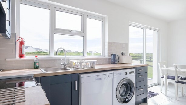 A modern kitchen with a built-in washing machine, a large window, and a view of the outdoors. - Clochan Na Mara 15 (In Liscannor Village) (County Clare)