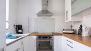 Une cuisine moderne avec des armoires blanches, une hotte de cuisinière en acier inoxydable, un four encastré, une machine à café et un grille-pain.