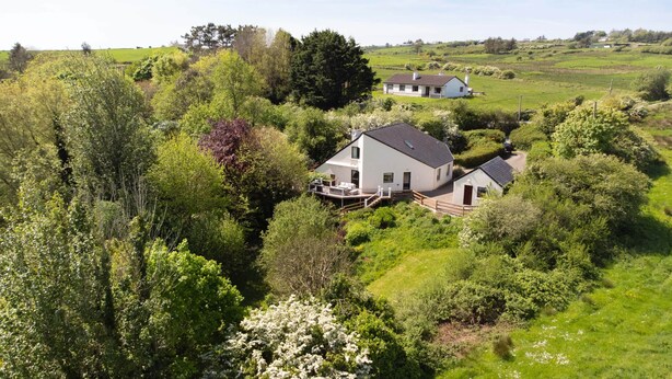 Une maison blanche dotée d’une terrasse, entourée d’une végétation luxuriante et de champs.