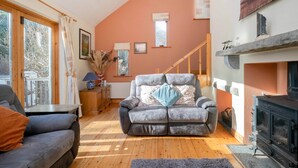 Un salon chaleureux avec une cheminée, un canapé, une table basse et une vue sur l’extérieur grâce à de grandes fenêtres.