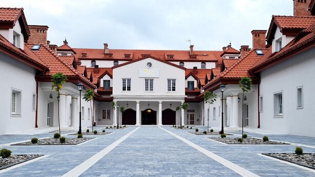 A building with a central entrance, flanked by two wings, and a paved courtyard with small trees. - Zielony Kompleks Dwór Ostoya (Trzebownisko)