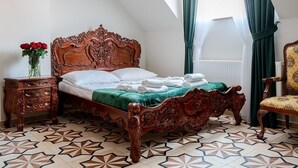 A room with a wooden bed, a nightstand with a vase of red roses, a patterned floor, and a chair with a floral upholstery. - Zielony Kompleks Dwór Ostoya (Trzebownisko)