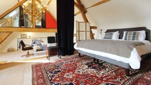 Ein Schlafzimmer mit einem großen Bett, einem Sessel, einem Schreibtisch und einem Teppich mit blau-rotem Muster.