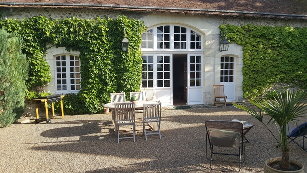 Ein rustikales Gebäude mit Kiesterrasse, Außenbestuhlung und Grill.