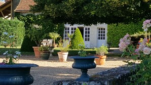 Ein Garten mit verschiedenen Blumentöpfen, ein weißes Gebäude mit Fenstern und eine Steinmauer.