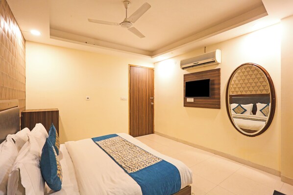 A hotel room with a bed, a ceiling fan, an air conditioning unit, a television, and a mirror.