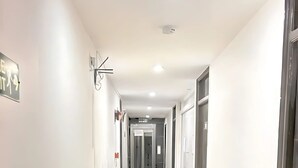 Un long couloir étroit aux murs blancs et au sol carrelé brillant, qui mène à une porte au fond.