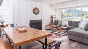 Un salon moderne avec une table à manger en bois, un canapé gris et une cheminée.