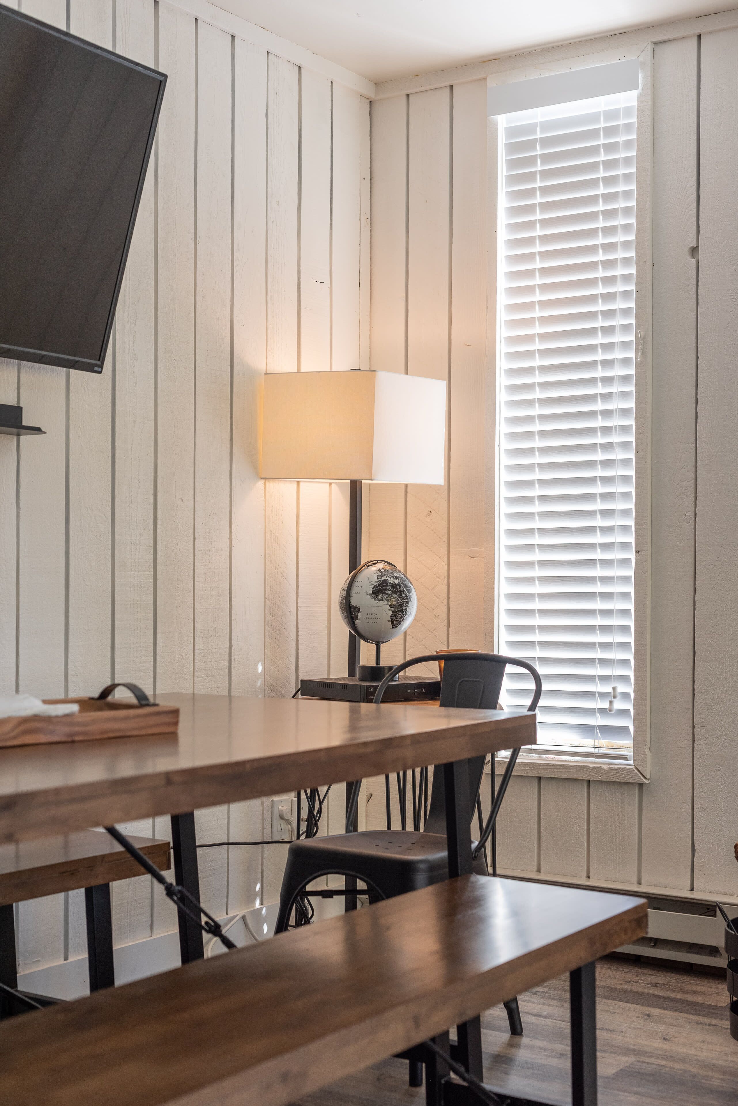 A room with a wooden table, a lamp, a globe, and a window with blinds.