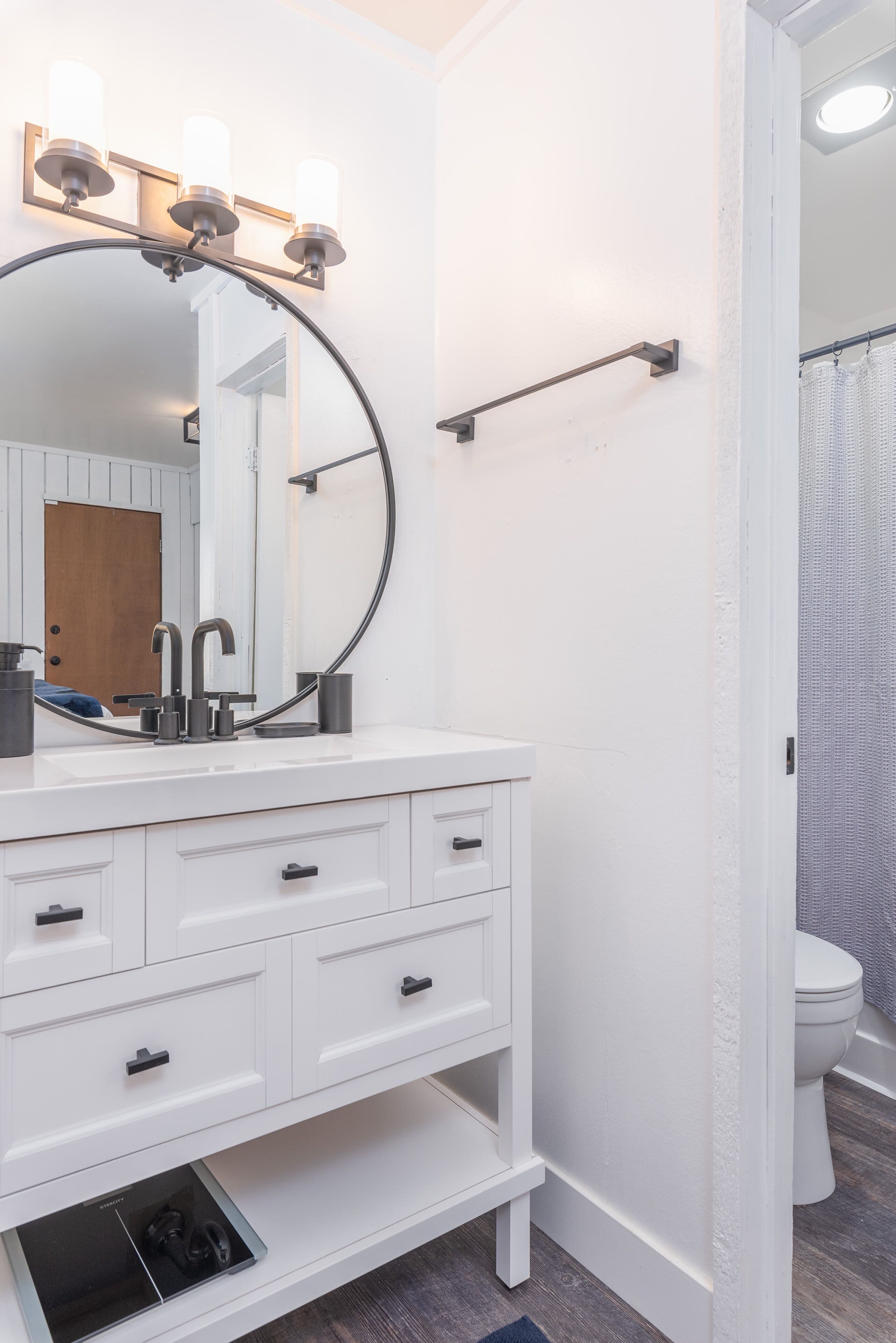 A bathroom with a white vanity, a round mirror, and three wall-mounted lights.