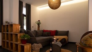 A modern living room with a sectional sofa, a wooden shelving unit, a globe, and a small round table with a candle and wine glasses. - NEU Luxus-apartment! Wasserbett-terrasse-smarttv (Magdeburg)