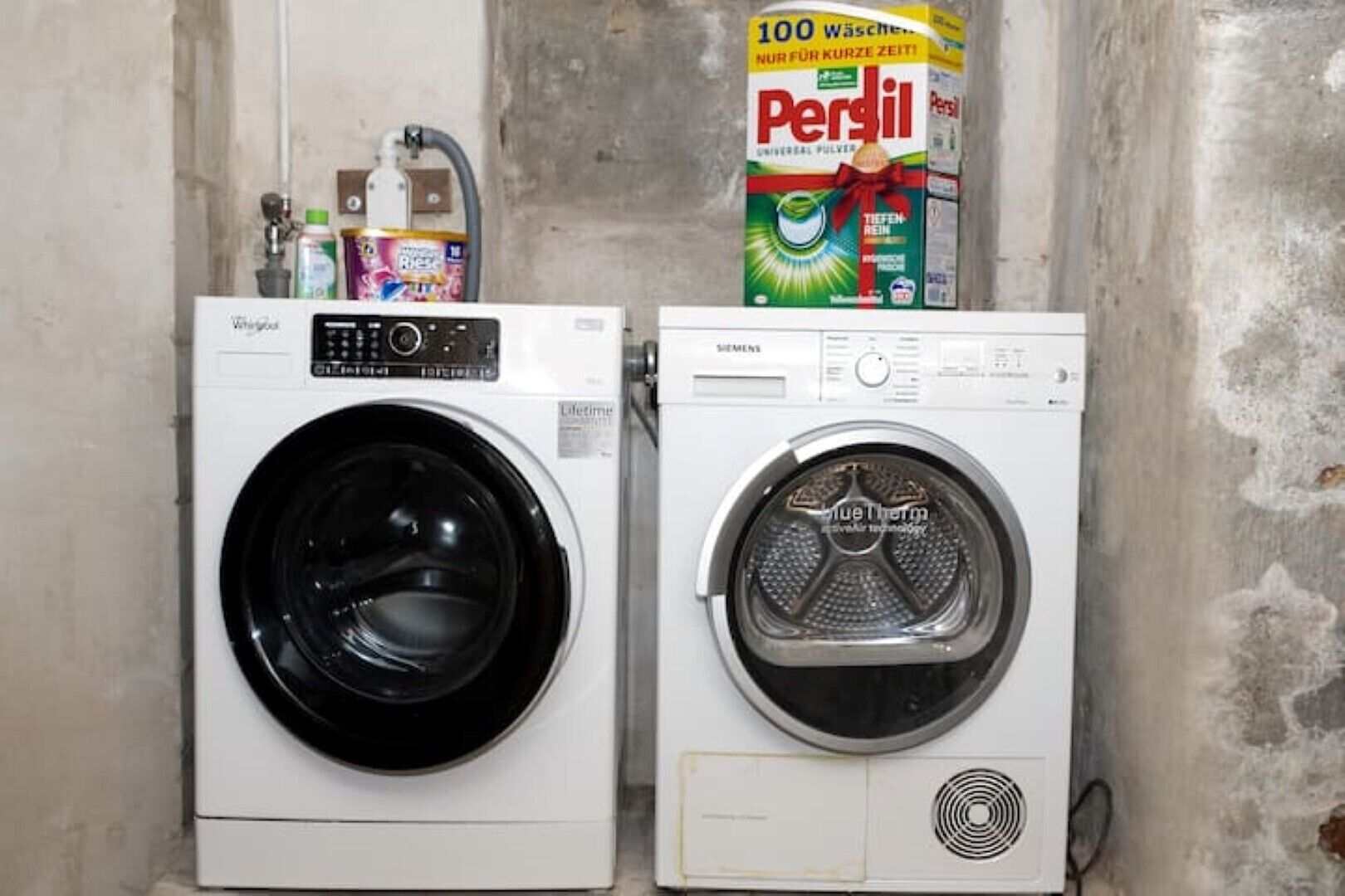 Two front-loading washing machines in a laundry room with a Persil detergent box visible in the background.