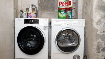 Two front-loading washing machines in a laundry room with a Persil detergent box visible in the background.