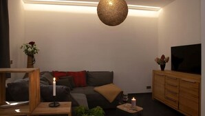 A modern living room with a sofa, a TV, a wooden cabinet, and a hanging light fixture. - NEU Luxus-apartment! Wasserbett-terrasse-smarttv (Magdeburg)