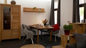 A modern living room with a dining area, wooden furniture, and a potted plant. - NEU Luxus-apartment! Wasserbett-terrasse-smarttv (Magdeburg)