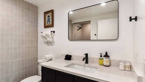 Un baño moderno con inodoro, lavabo y espejo. Hay toallas y artículos de aseo en la encimera.