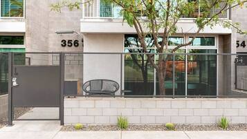A modern building with a gated entrance, numbered units, and a small seating area with a chair and table.