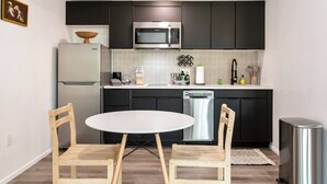 A compact kitchen with dark cabinets, a stainless steel microwave, a dishwasher, and a small round table with wooden chairs. - Jupiter's Studio Apartment with Pool!!! (Tempe)
