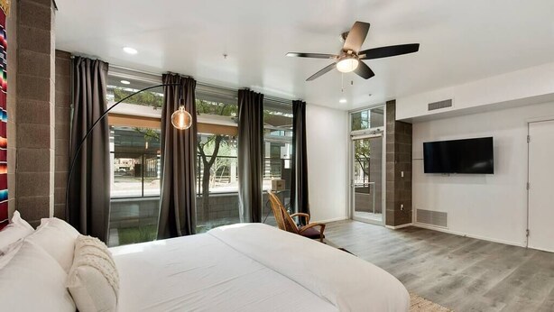 A modern bedroom with a large bed, a ceiling fan, a TV, and a view of the outdoors. - Jupiter's Studio Apartment with Pool!!! (Tempe)