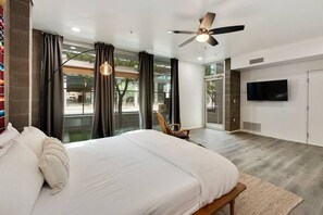 A modern bedroom with a large bed, a ceiling fan, a TV, and a view of the outdoors. - Jupiter's Studio Apartment with Pool!!! (Tempe)