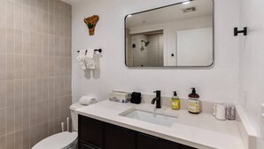 A modern bathroom with a white sink, dark cabinets, a large mirror, and toiletries on the counter. - Jupiter's Studio Apartment with Pool!!! (Tempe)