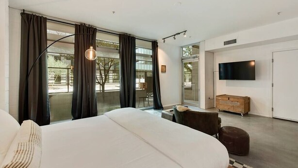 Ein modernes Schlafzimmer mit einem großen Bett, einem an der Wand montierten Fernseher und Blick ins Freie durch große Fenster.