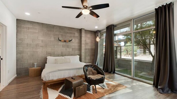 A modern bedroom with a large bed, a ceiling fan, a view of the outdoors, and a rustic rug.