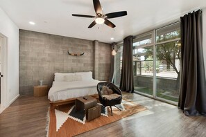 Une chambre moderne avec un grand lit, un ventilateur de plafond, une vue sur l’extérieur et un tapis au style rustique.